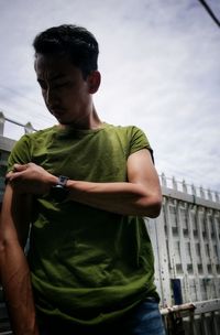 Young man looking away while standing against sky