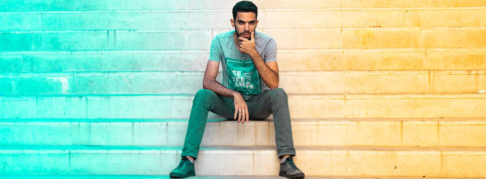 Young man using mobile phone while sitting on wall