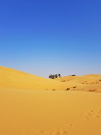 Scenic view of desert against clear blue sky and an oasis