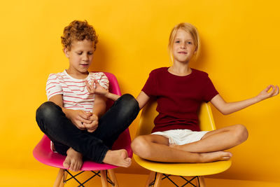 Portrait of happy friends sitting on chair against yellow background