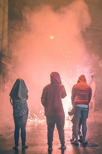 Rear view of people standing on street by firework at night