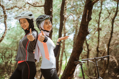 Portrait of young female friends standing against trees