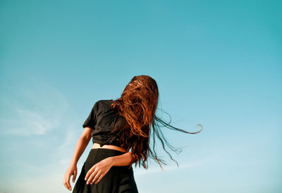 Low angle view of woman tossing hair against clear sky