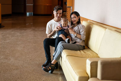 Asian muslim couple with one year old baby daughter, at long light brown sofa, long hair, portrait
