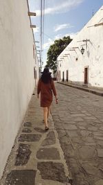 Rear view of woman walking on footpath amidst buildings in city