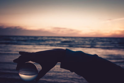 Man holding umbrella at beach against sky during sunset