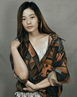 Portrait of young woman standing against gray background