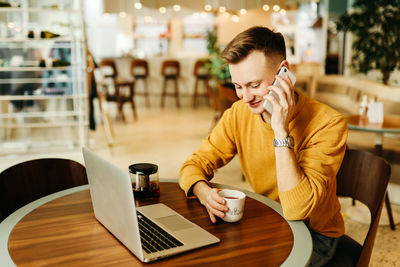 Young woman using phone while sitting at table