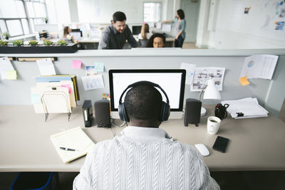 Rear view of businessman working on desktop computer with colleagues in background