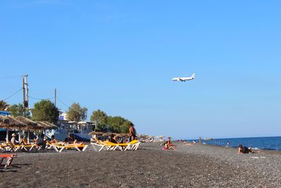 Birds flying over beach against clear blue sky