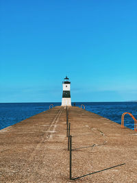 Lighthouse by sea against clear blue sky