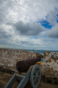 Old rusty wheel by sea against sky