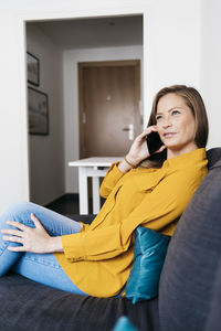 Young woman talking over mobile phone while sitting on sofa at home