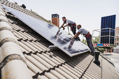 Craftsmen installing solar panels on rooftop of house