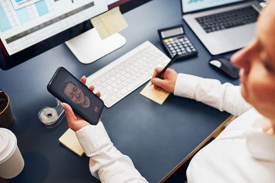 Woman entrepreneur having business video chat on smartphone. woman making notes while talking