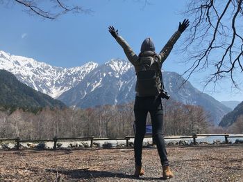 Rear view of woman standing with arms outstretched against mountain range during winter