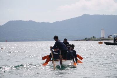 Rear view of men on boat in sea against sky