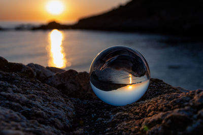 Close-up of crystal ball on rock at beach during sunrise 