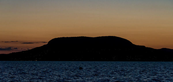 Silhouette of person swimming in sea against sunset sky