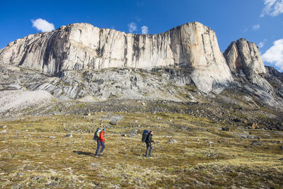 Two backpackers traverse below baffin island mountains.