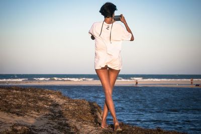 Full length rear view of woman photographing sea through smart phone