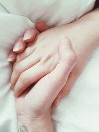 Close-up of people holding hands on bed