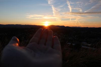 Close-up of hands against sky during sunset