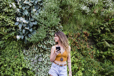 Young woman using phone while standing on plants