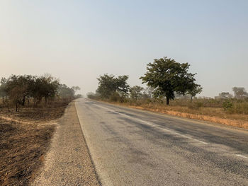 Road by trees against clear sky