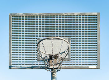 Low angle view of metallic basketball hoop against blue sky on sunny day