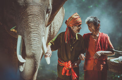 Senior couple standing by elephant in forest