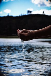 Cropped image of person with hands cupped over lake against sky