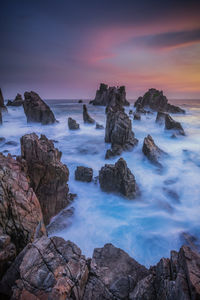 Rocks in sea against sky during sunset