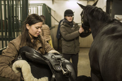 Young couple preparing horse in stable