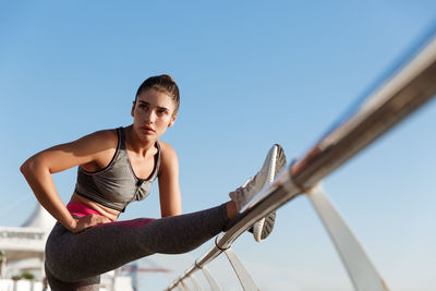 Low angle view of woman exercising against clear blue sky