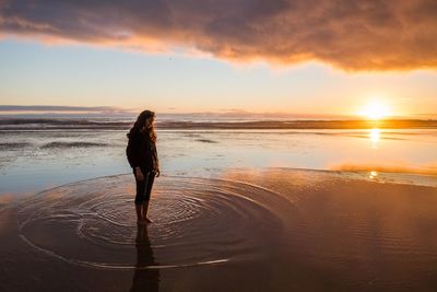 Full length of woman standing at beach against sky during sunset