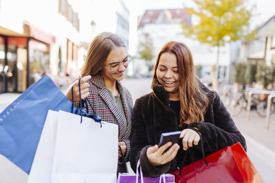 Happy woman sharing mobile phone with friend