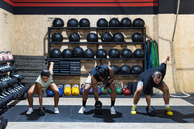 Full body of strong hispanic sportspeople in sportswear lifting heavy kettlebells during weightlifting workout near weights in light modern gym