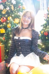 Portrait of young woman standing against christmas tree