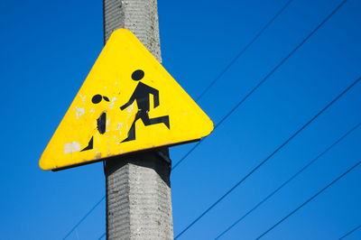 Low angle view of yellow road sign against blue sky on sunny day