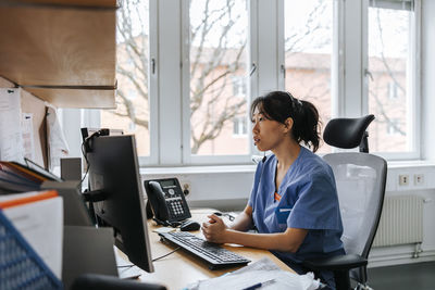 Female medical professional sitting on chair and doing online consultation on video call through computer at clinic