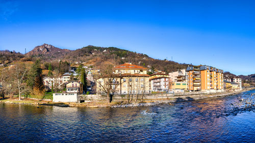 Buildings by river against clear blue sky