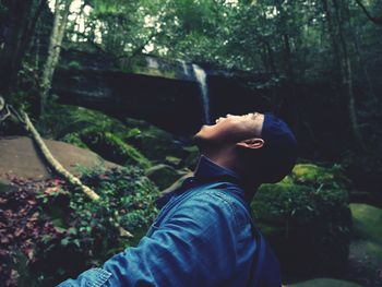 Man standing with mouth open against waterfall in forest 