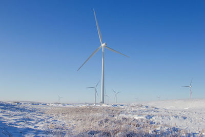 Wind turbines on snowy field against clear blue sky