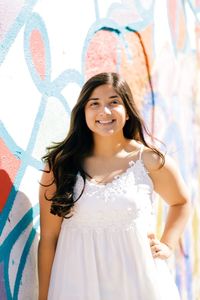 Portrait of smiling young woman standing against wall