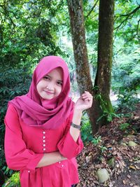 Portrait of smiling young woman standing against trees in forest