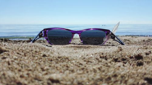 Surface level of purple sunglasses with feather on shore against clear sky