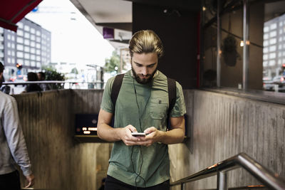 Man using mobile phone while walking up on steps at subway station in city