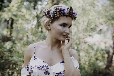 Close-up of young woman wearing flowers against trees