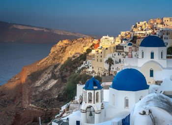 Buildings by sea against clear blue sky